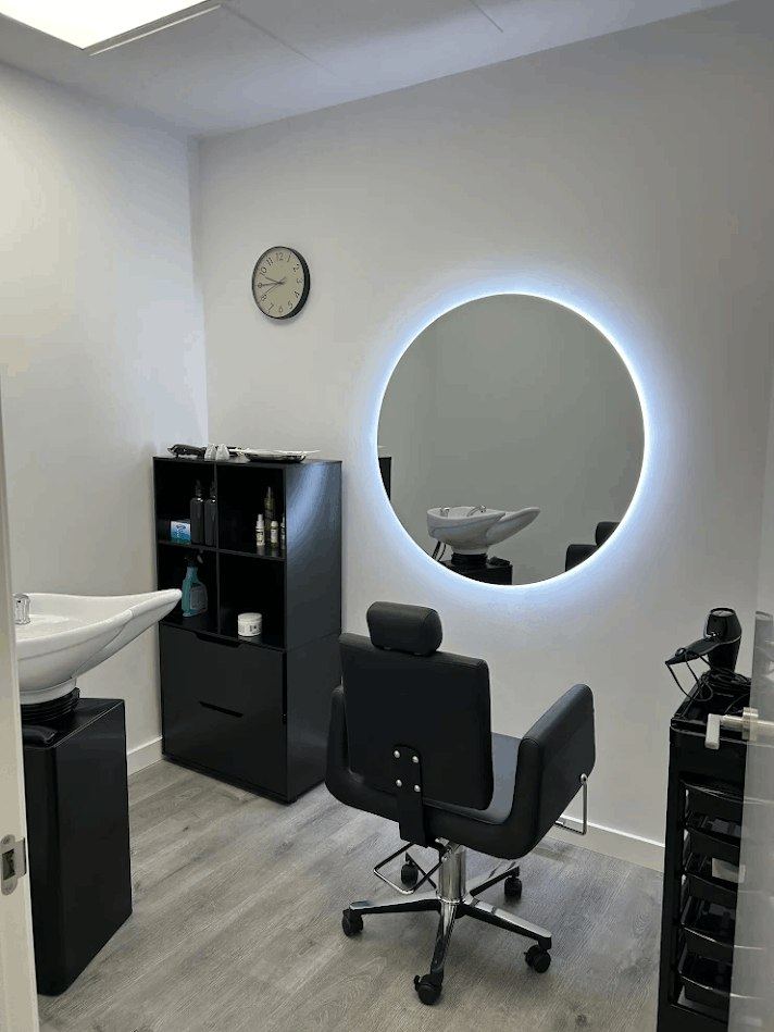 Puesto de trabajo del centro capilar Superhairpieces en Madrid: sillón, espejo redondo retroiluminado y lavacabezas.