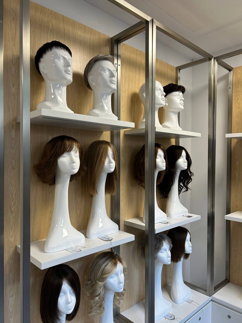 Sala de exposición con pelucas y prótesis capilares expuestas en cabezas de maniquí.