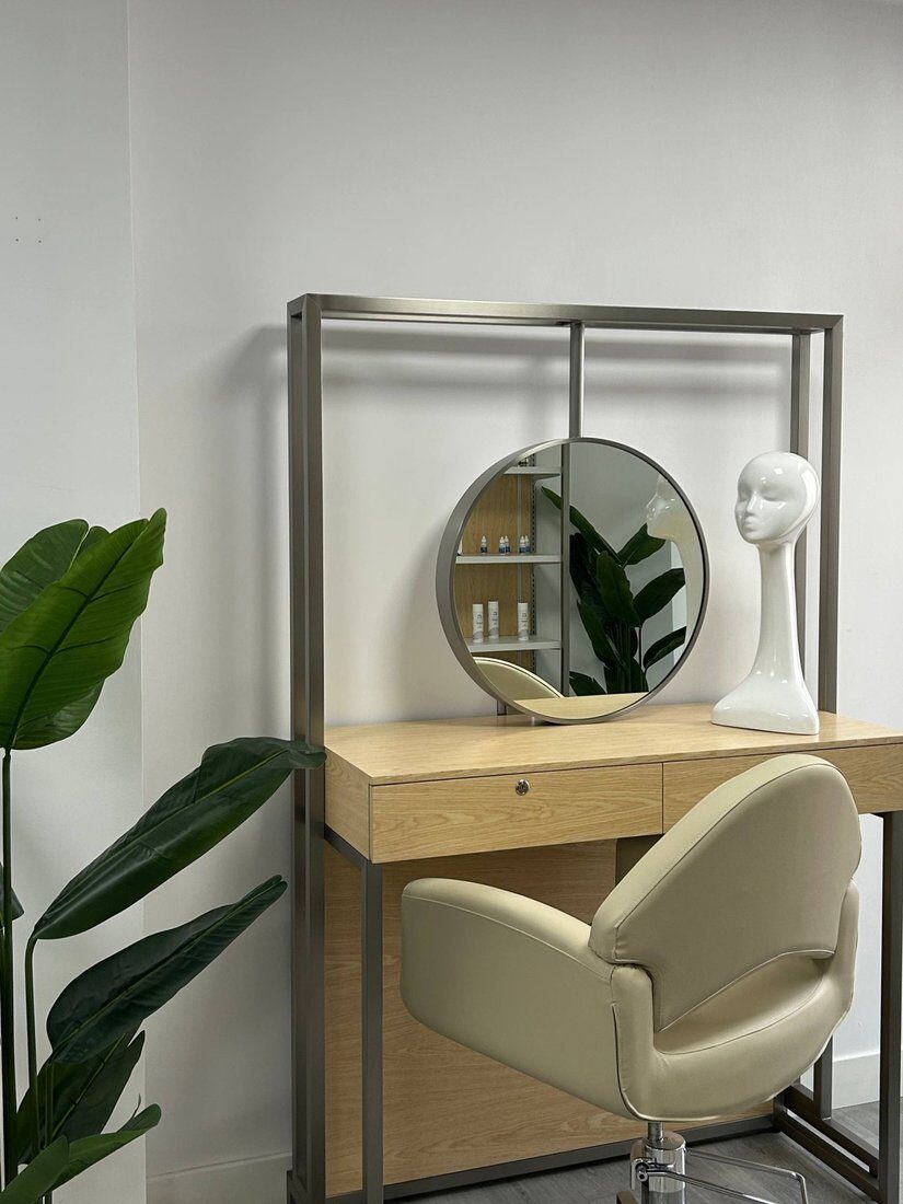 Tocador del salón con espejo redondo, sillón y planta.